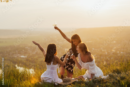 Cute girls on the hill on the grass have fun, have a good time, are happy. Young happy woman female friends having picnic on nature. Happy life concept. Copy space.
