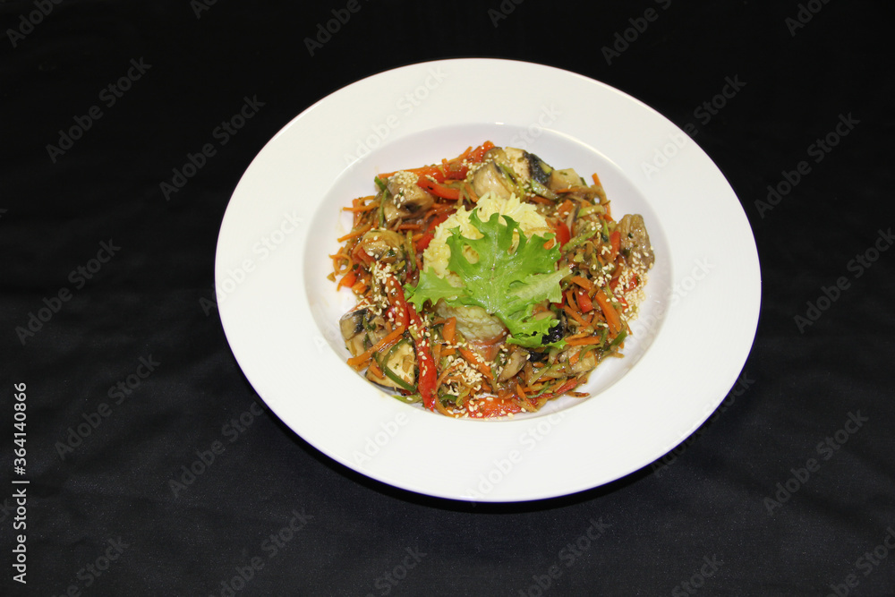 Rice covered with salad leaf and salad of mushrooms, seaweed, pepper and carrots on a white plate. Close-up