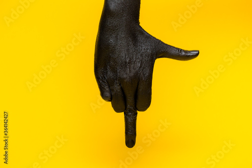 Elegant female hand with a black paint on it shows middle finger isolated on a yellow background. Free space for text 