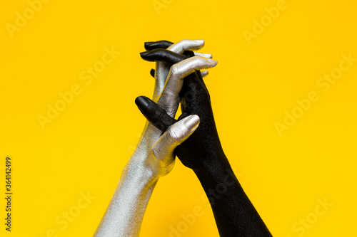 Elegant female hands with a silver and black paint on them keeps together isolated on a yellow background. Free space for text