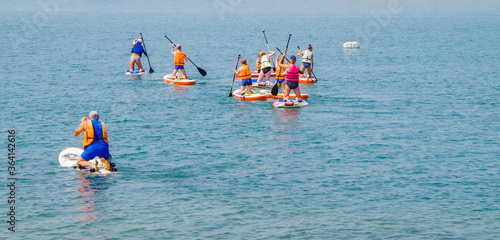group of surfers on boards for sap surfing with oars have fun together, concept of active lifestyle © Sergey