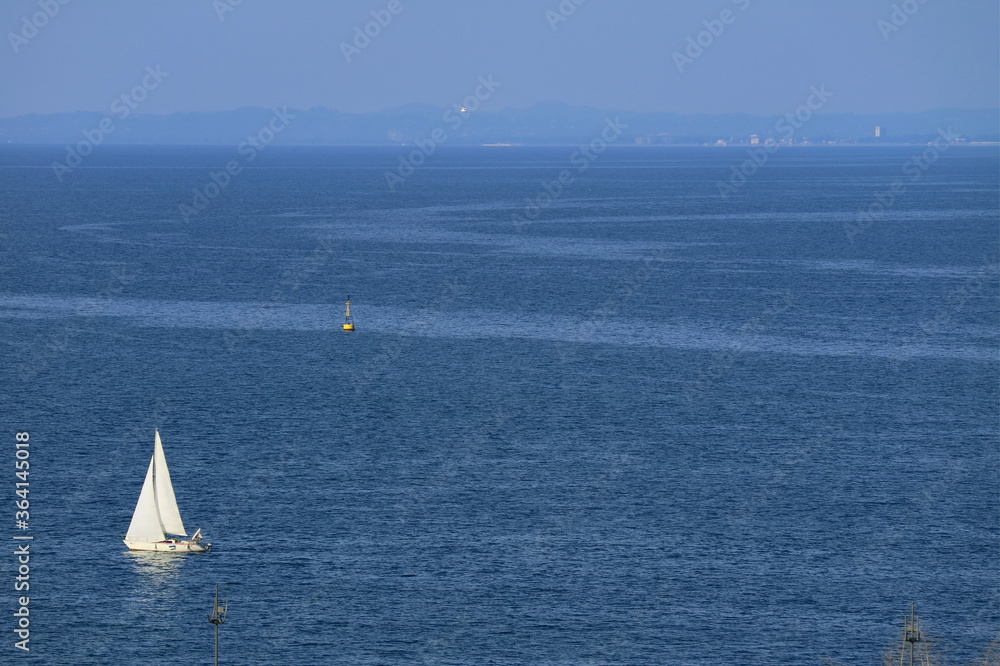 Panoramic aerial view of a white sailboat on the blue calm sea 	