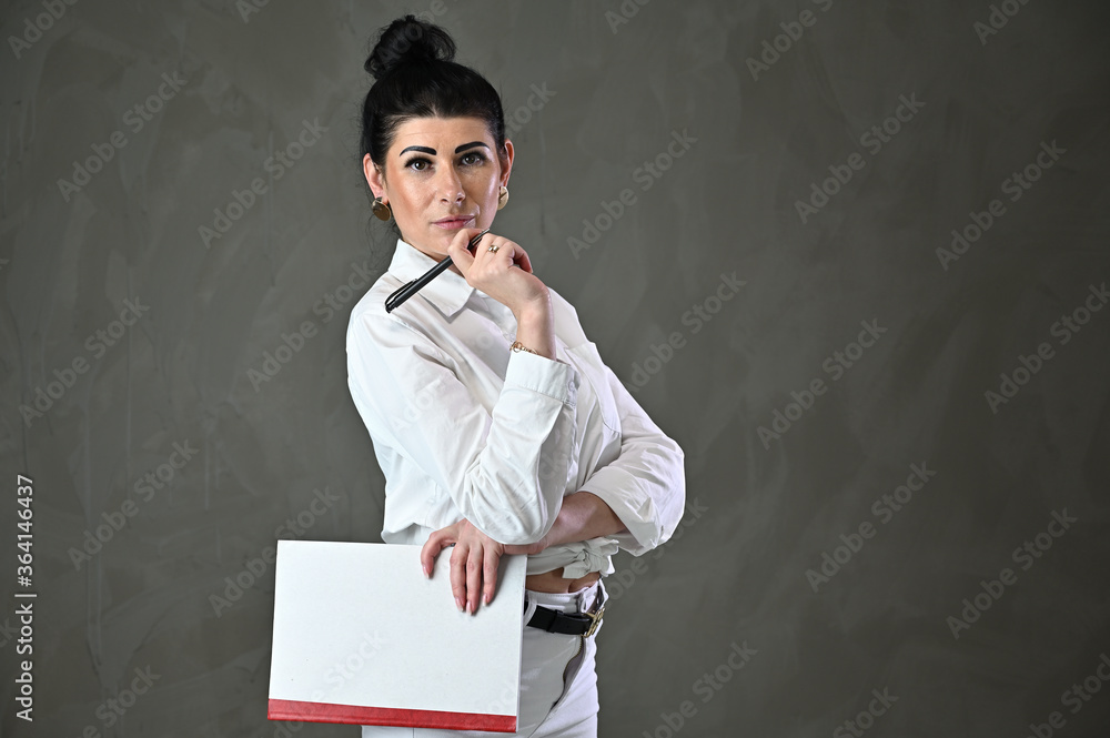 Studio portrait of a caucasian woman brunette manager with a folder in hands on a gray background Studio portrait of a caucasian woman brunette manager with a folder in hands on a gray background