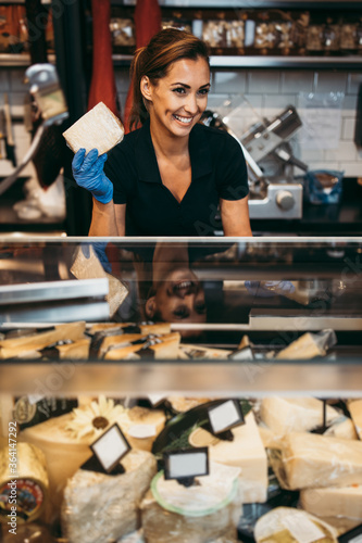 Foto Beautiful and happy female seller working in supermarket or grocery store and selling cured meat products and cheeses