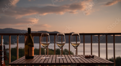 Three glasses of white wine on a wooden table, on a veranda with a beautiful view of the Mediterranean