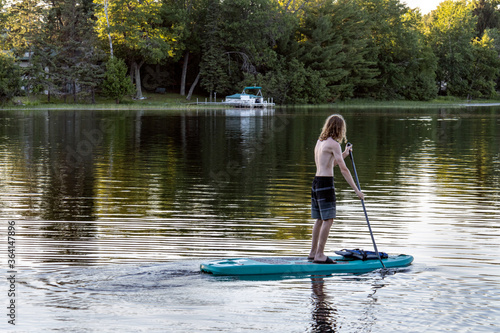 Teenage boy paddle boarding on lake © Bill Keefrey