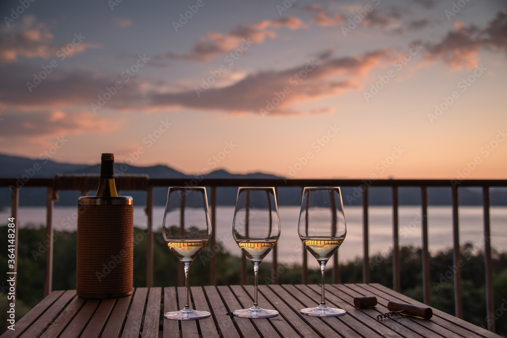 Three glasses of white wine on a wooden table, on a veranda with a beautiful view of the Mediterranean