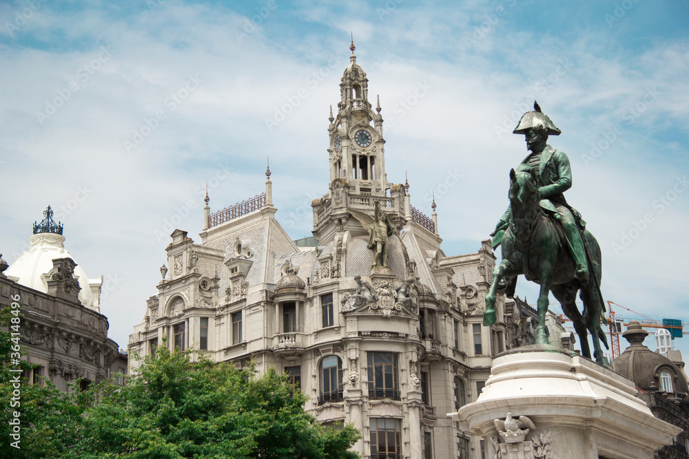 Liberty square in the historic center of Porto with statue of King Pedro IV on top of a horse in front in the foreground with a majestic building during a very sunny day in Portugal