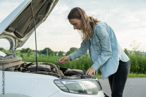 Woman standing near the broken car. The girl opened the hood and look at the engine. 
