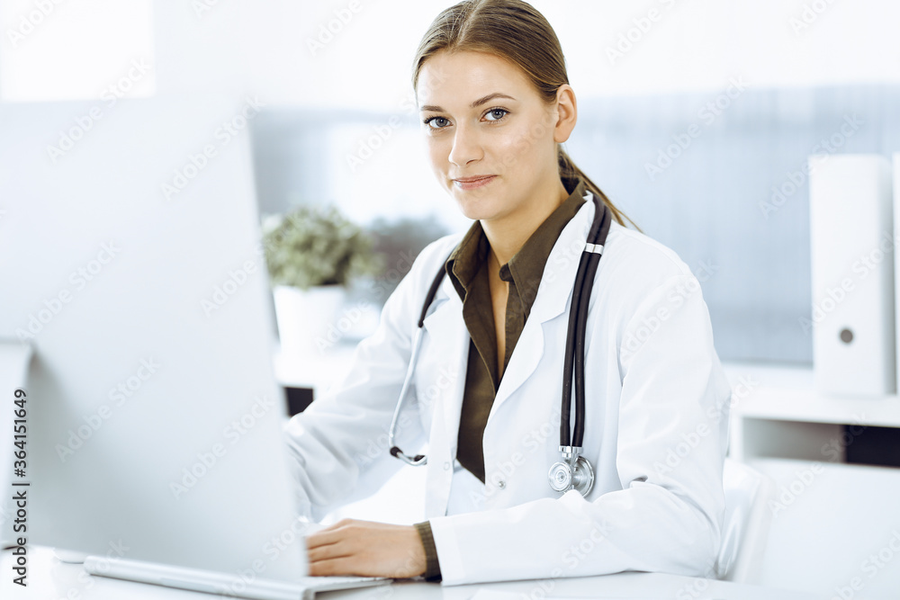 Woman-doctor typing on pc computer while sitting at the desk in hospital office. Data in medicine and healthcare Woman-doctor typing on pc computer while sitting at the desk in hospital office. Data in medicine and healthcare