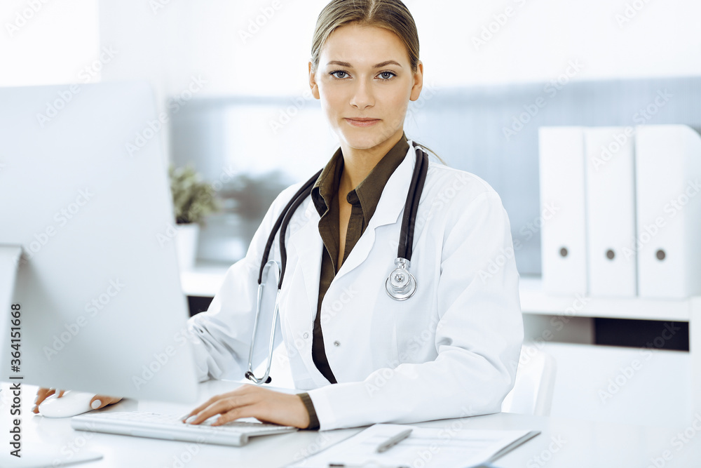 Woman-doctor typing on pc computer while sitting at the desk in hospital office. Data in medicine and healthcare Woman-doctor typing on pc computer while sitting at the desk in hospital office. Data in medicine and healthcare