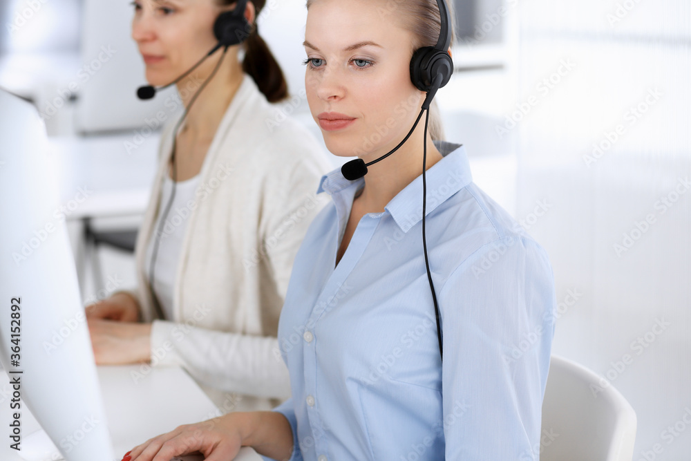 Call center office. Beautiful blonde woman using computer and headset for consulting clients online. Group of operators working as customer service occupation. Business people concept Call center office. Beautiful blonde woman using computer and headset for consulting clients online. Group of operators working as customer service occupation. Business people concept