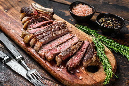 Grilled cowboy or rib eye beef steak with herbs and spices.  Wooden dark background. Top view.