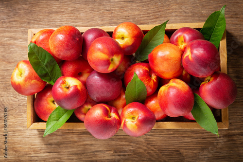 fresh nectarines with leaves in a wooden box, top view