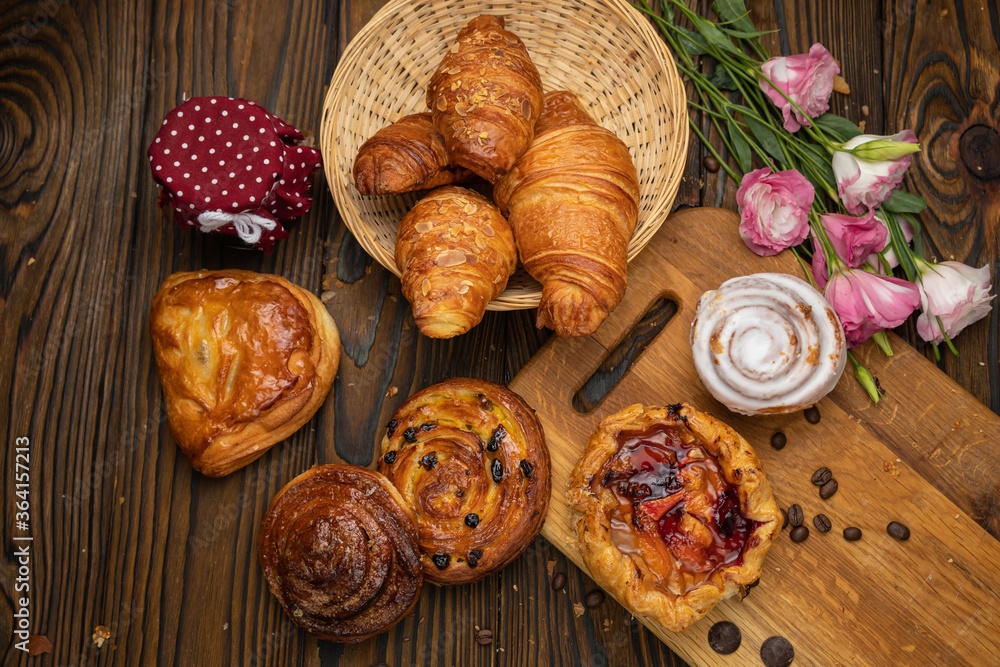 Assorted pastries, croissants, buns. On a brown wooden table.
