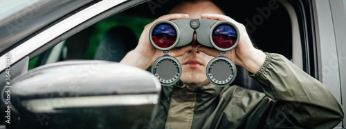 Canvas Print Panorama a young hunter is sitting in the car and looks into the binoculars