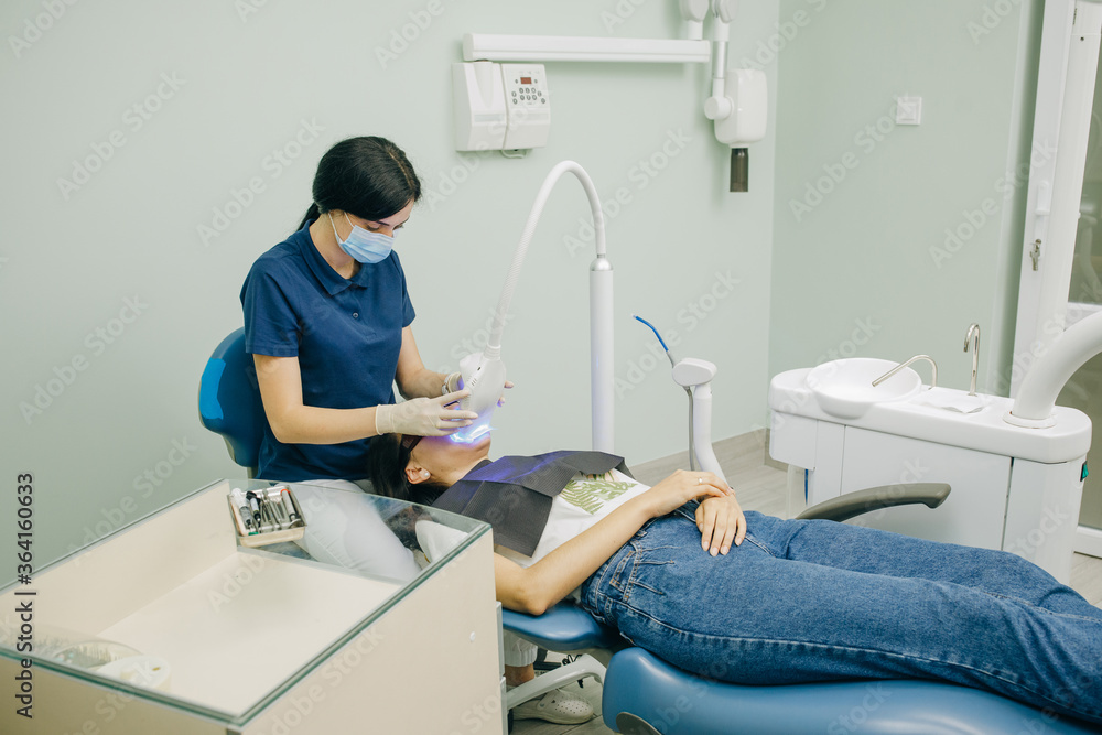 Obraz premium Dentist stomatologist whitening teeth for patient in medicine dental clinic with lamp. Concept of teeth care and dentistry. Teeth whitening procedure