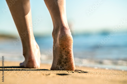 Close up of woman feet walking barefoot on sand leaving footprints on golden beach. Vacation, travel and freedom concept. People relaxing in summer.