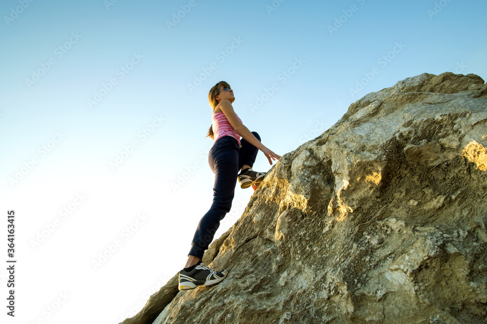 Woman hiker climbing steep big rock on a sunny day. Young female climber overcomes difficult climbing route. Active recreation in nature concept. Woman hiker climbing steep big rock on a sunny day. Young female climber overcomes difficult climbing route. Active recreation in nature concept.
