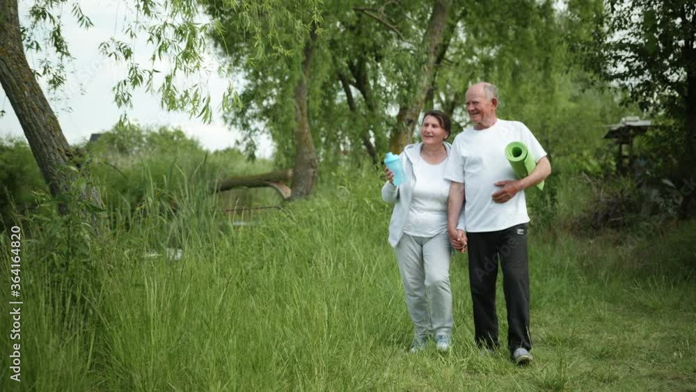 healthy old people male and female married couple take care of their health go holding hands after morning workout outdoors near river among reeds healthy old people male and female married couple take care of their health go holding hands after morning workout outdoors near river among reeds