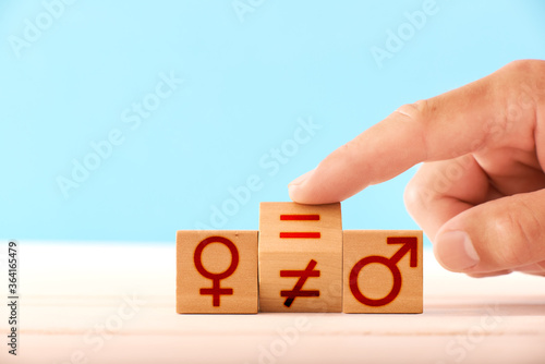 gender equality concept. a man flips a wooden block and changes the equal sign to an inequality between the man and woman icons