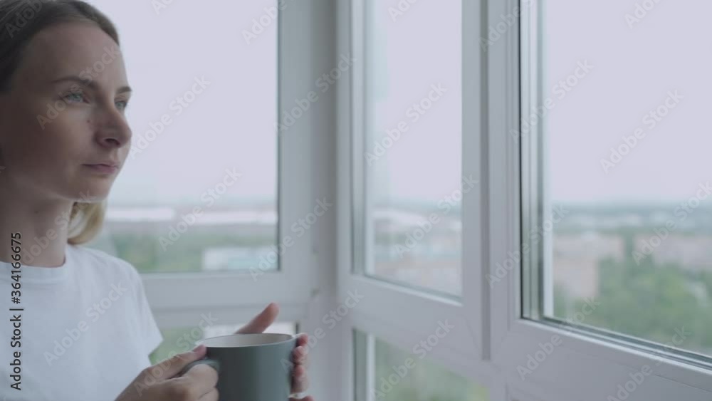 Woman looking out window enjoying fresh new day feeling rested and drinking coffee at home. Slow Motion Woman looking out window enjoying fresh new day feeling rested and drinking coffee at home. Slow Motion