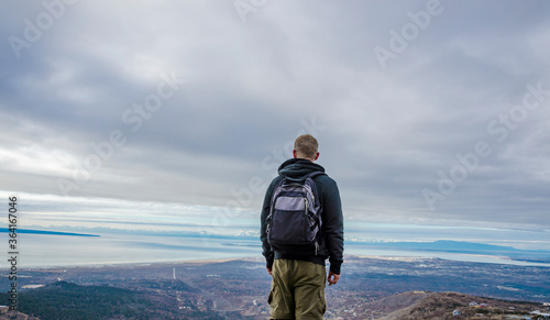 Adventurous man standing on top of a lookout platform looking at the open landscape on a cloudy day.