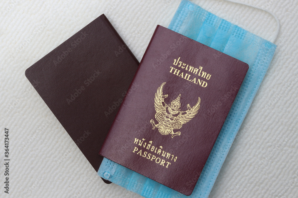 Thai Passport with medical face mask on white background with copy space. Lifestyle and traveling concept in New Normal after Covid-19 / Coronavirus pandemic. Thai Passport with medical face mask on white background with copy space. Lifestyle and traveling concept in New Normal after Covid-19 / Coronavirus pandemic.