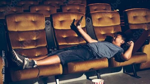 A boy laying down and playing a game and take a photo in the cinema photo