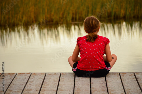 Canvas Print Girl sitting alone on dock facing marsh reeds