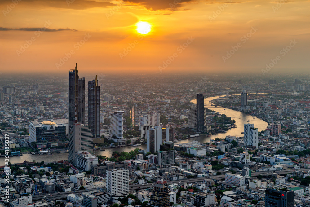 Skyscraper Buildings along curve of Chao Phraya River at Sunset with Orange Sky, Bangkok, Thailand