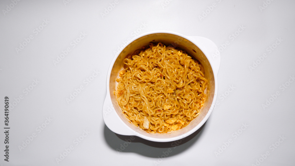 A tasty instant fried noodle (Indomie Goreng) mixed with scrambled boiled egg in a white bowl. Top view of delicious fried noodle