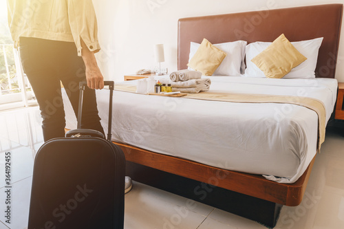 Cropped view of tourist woman hand pulling her luggage in hotel bedroom after check-in.