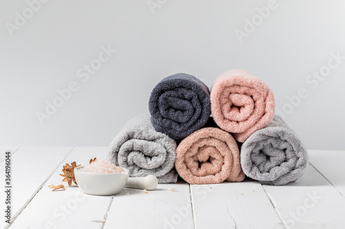Stack of rolled cotton towels with a bowl of bath salts on gray background, copy space.