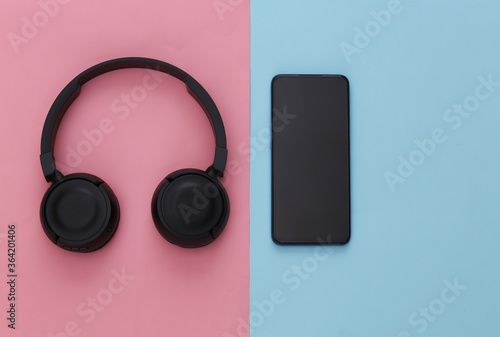 Smartphone with black stereo headphones on pink blue pastel background. Top view