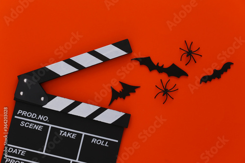 Horror movie, halloween theme. Movie clapperboard, spiders and flying decorative bats on orange background. Top view, flat lay photo