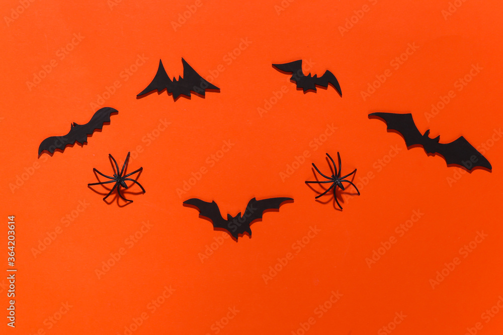 Halloween background, decorations and scary concept. Spiders and black bats fly over bright orange background. Top view Halloween background, decorations and scary concept. Spiders and black bats fly over bright orange background. Top view