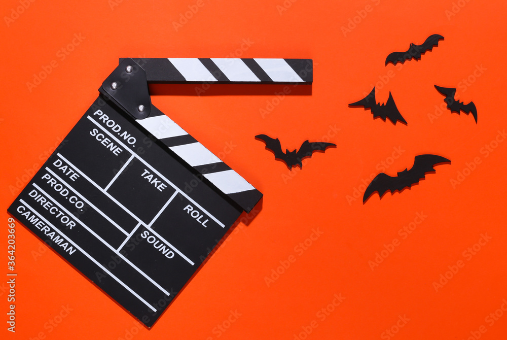 Naklejka premium Horror movie, halloween theme. Movie clapperboard and flying decorative bats on brightorange background. Top view, flat lay
