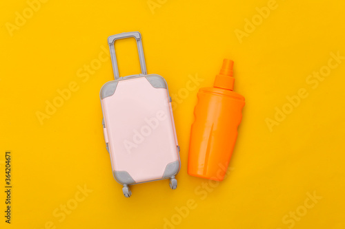 Beach vacation, travel concept. Mini toy travel luggage and sunblock bottle on yellow background. Top view. Flat lay