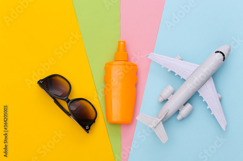 Beach vacation, travel concept. Sunblock bottle, air plane and camera on colored background. Top view. Flat lay