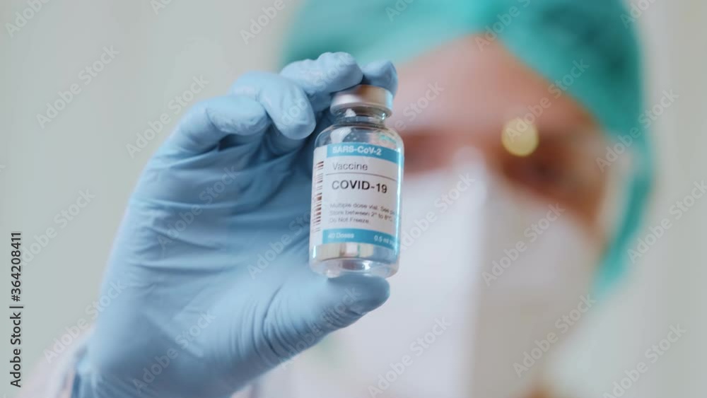 Doctor in protective hazmat suit shows bottle with Covid-19 vaccine in liquid. Scientists created vaccine, injection ready to test. Nurse in clinic laboratory. Vaccine development against coronavirus Doctor in protective hazmat suit shows bottle with Covid-19 vaccine in liquid. Scientists created vaccine, injection ready to test. Nurse in clinic laboratory. Vaccine development against coronavirus
