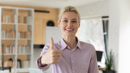 Headshot portrait of smiling Caucasian young businesswoman look at camera show thumb up recommend good quality service, happy female employee give recommendation to company training or course