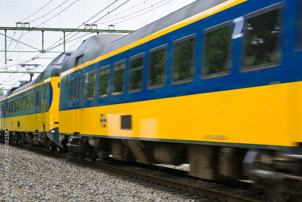 Dutch double-deck regional train with distinctive yellow and blue color and large windows passing by on a railway in Heerenveen in the Netherlands