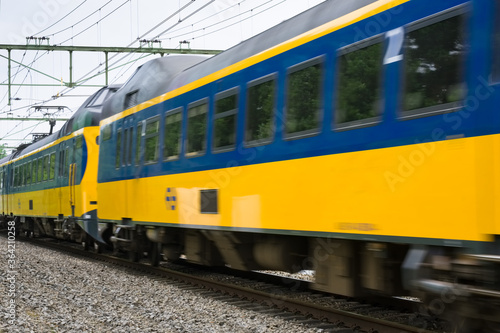 Dutch double-deck regional train with distinctive yellow and blue color and large windows passing by on a railway in Heerenveen in the Netherlands