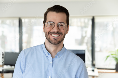 Headshot portrait of smiling confident young Caucasian businessman in glasses posing in office, happy excited male employee worker in spectacles show optimism success in work, employment concept