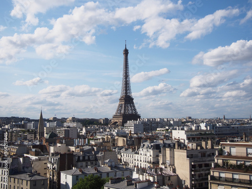 Paris skyline with the Eiffel Tower shining during the day when clouds seem to float comfortably in the blue clear sky.