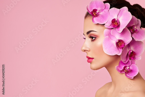 Portrait of beautiful young woman with orchid. Brunette woman with luxury makeup. Perfect skin. Eyelashes. Cosmetic eyeshadow. Purple flowers