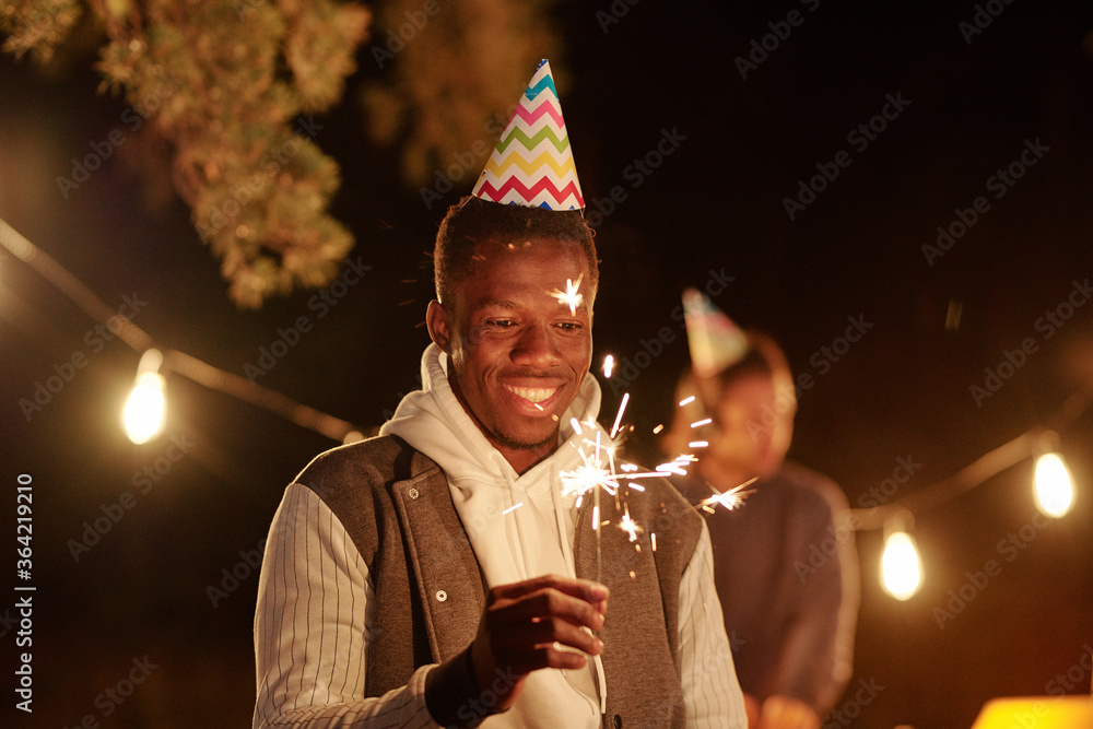 Happy young African man in birthday cap and casualwear holding Bengal light