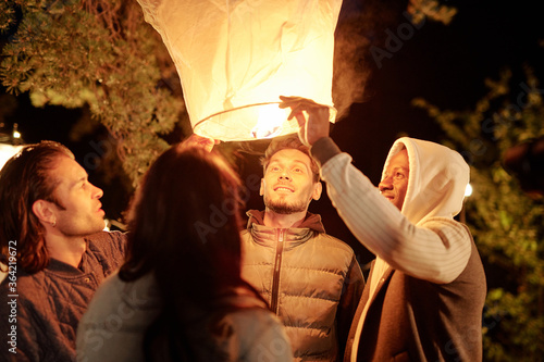 Young intercultural men and woman looking into illuminated large white balloon