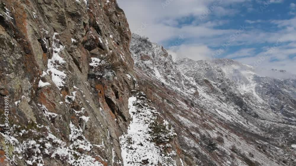 Aerial view of the close span of the camera next to a rock wall high in the mountains in early spring green grass and snow on the slopes of the mountains Aerial view of the close span of the camera next to a rock wall high in the mountains in early spring green grass and snow on the slopes of the mountains